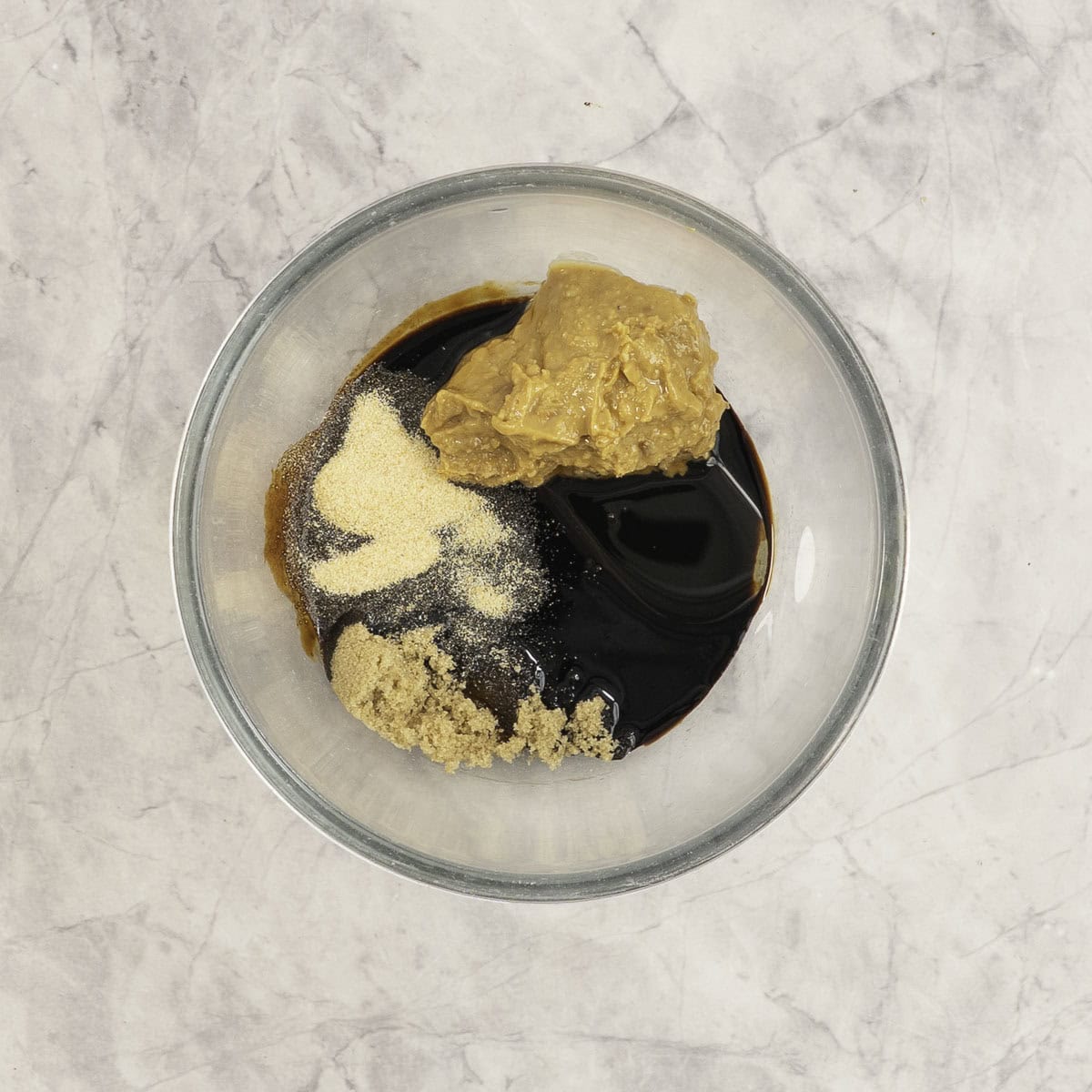 Sauce ingredients in a glass bowl on marble bench top.