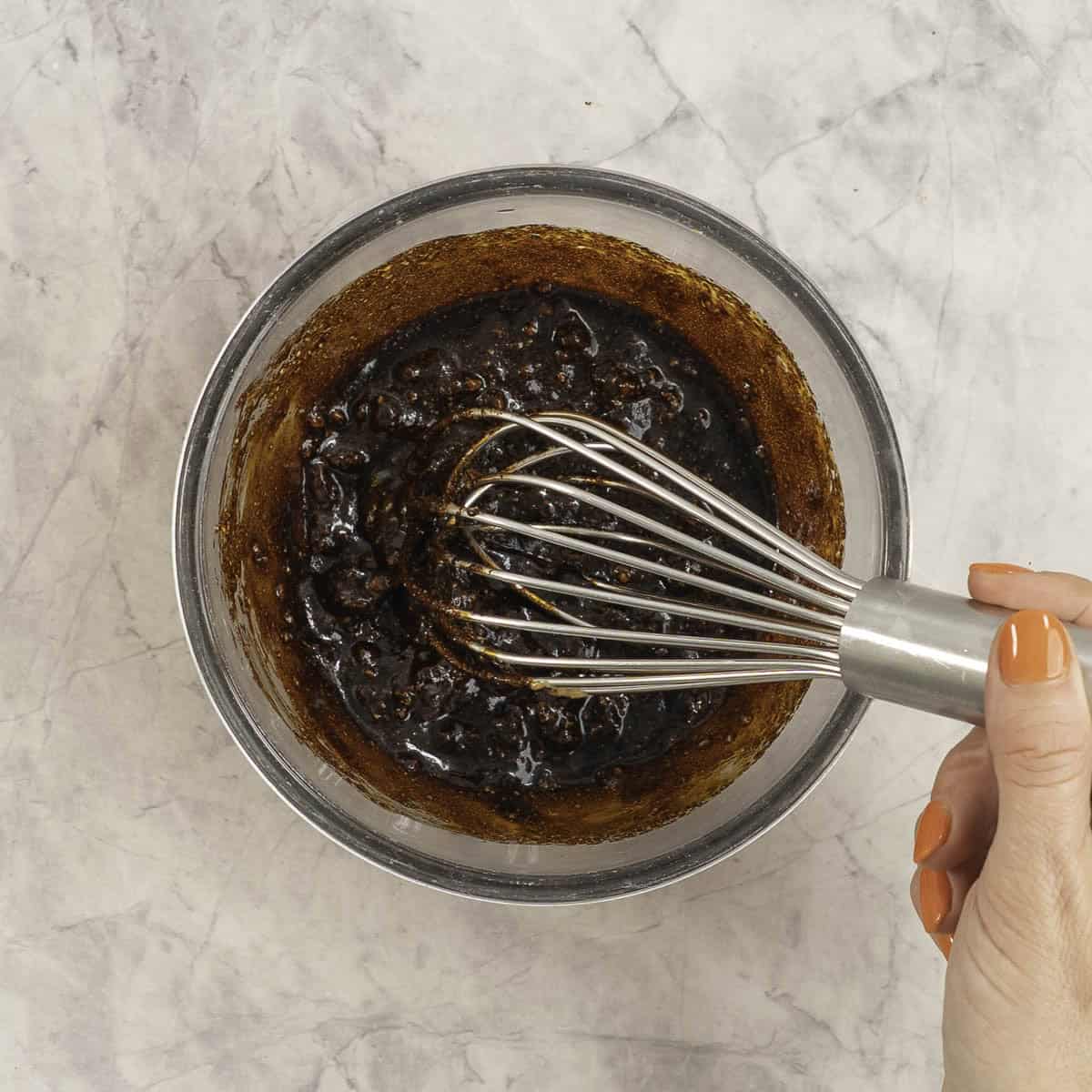 Mixture of sauce ingredients being stirred together with a metal whisk.