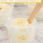 Banana yogurt with banana slices in a small glass bowl with toddler spoon, text overlay; 'Banana Yogurt, healthy toddler snack'.