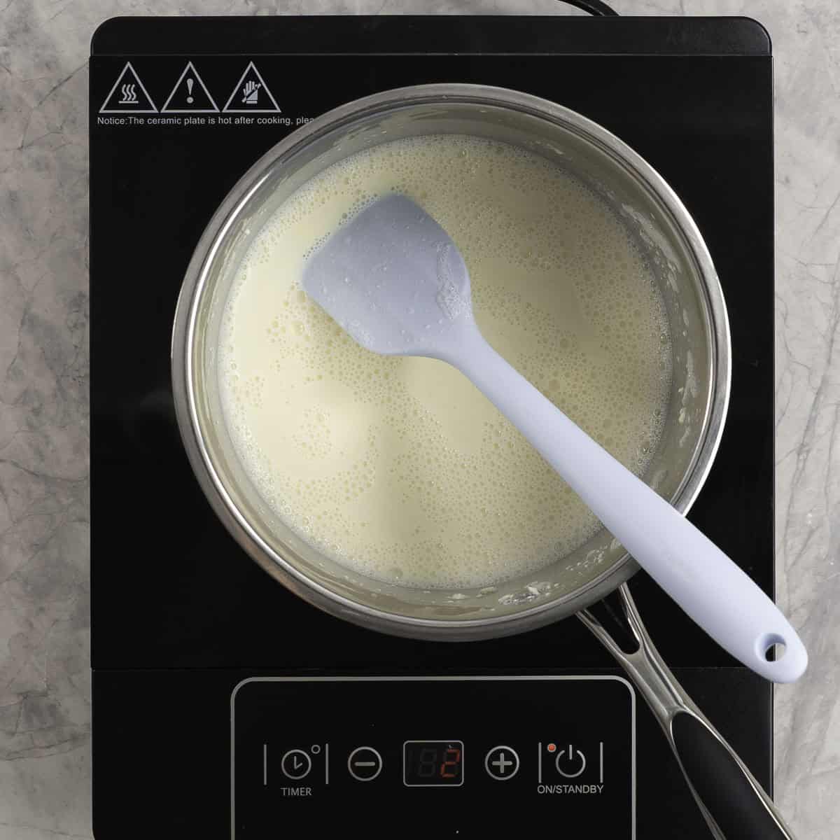 Milk mixture simmering on stove top with spatula inside.