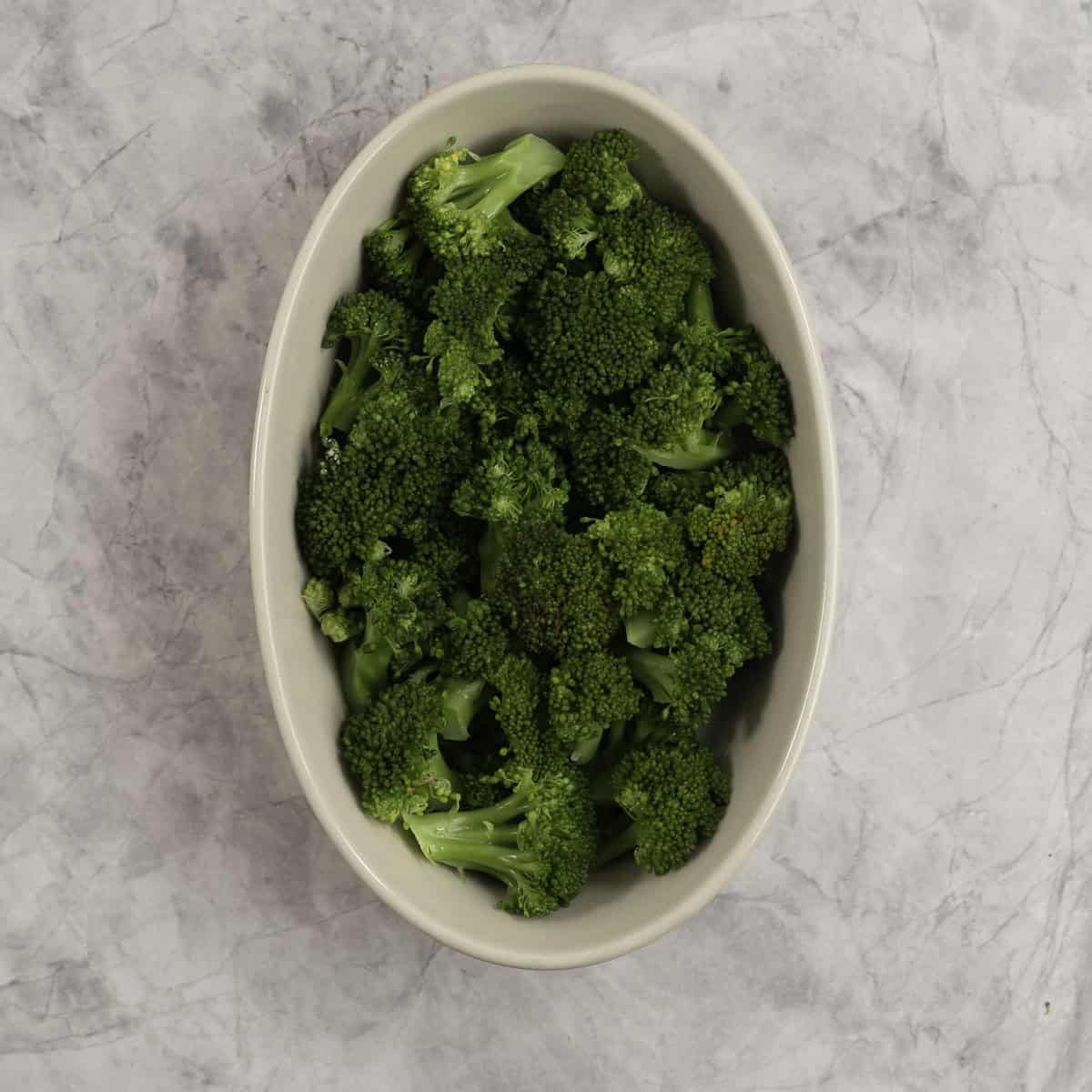 Broccoli florets in a oval casserole dish on marble benchtop.