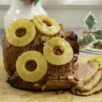 Golden glossy ham with pineapple rings placed on top, three pieces sliced from ham.