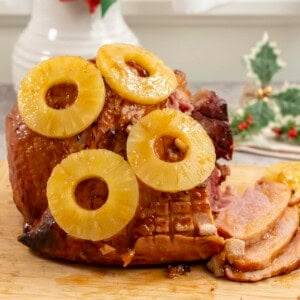 Golden glossy ham with pineapple rings placed on top, three pieces sliced from ham.