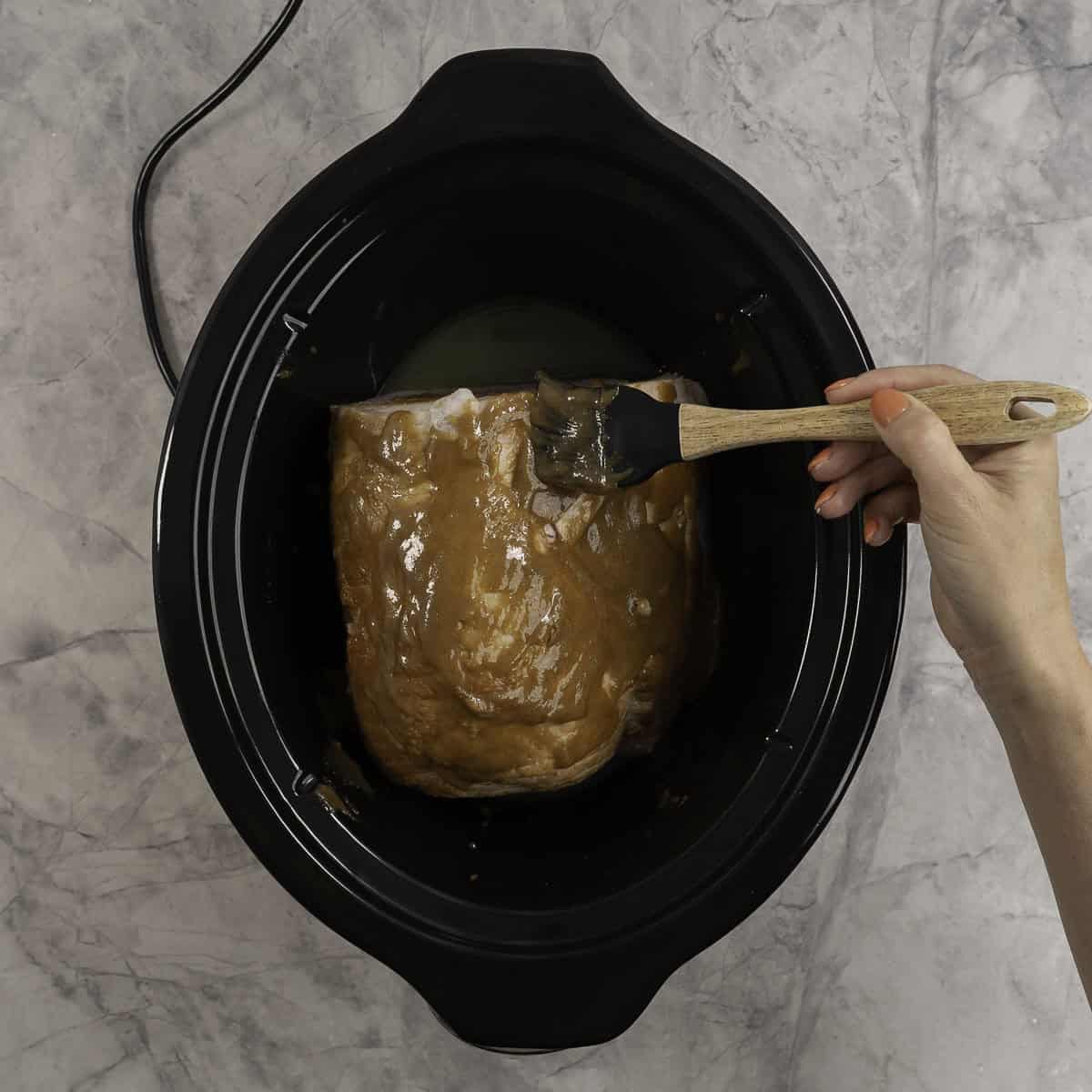 Woman holding a basting brush applying brown sugar mixture on ham.