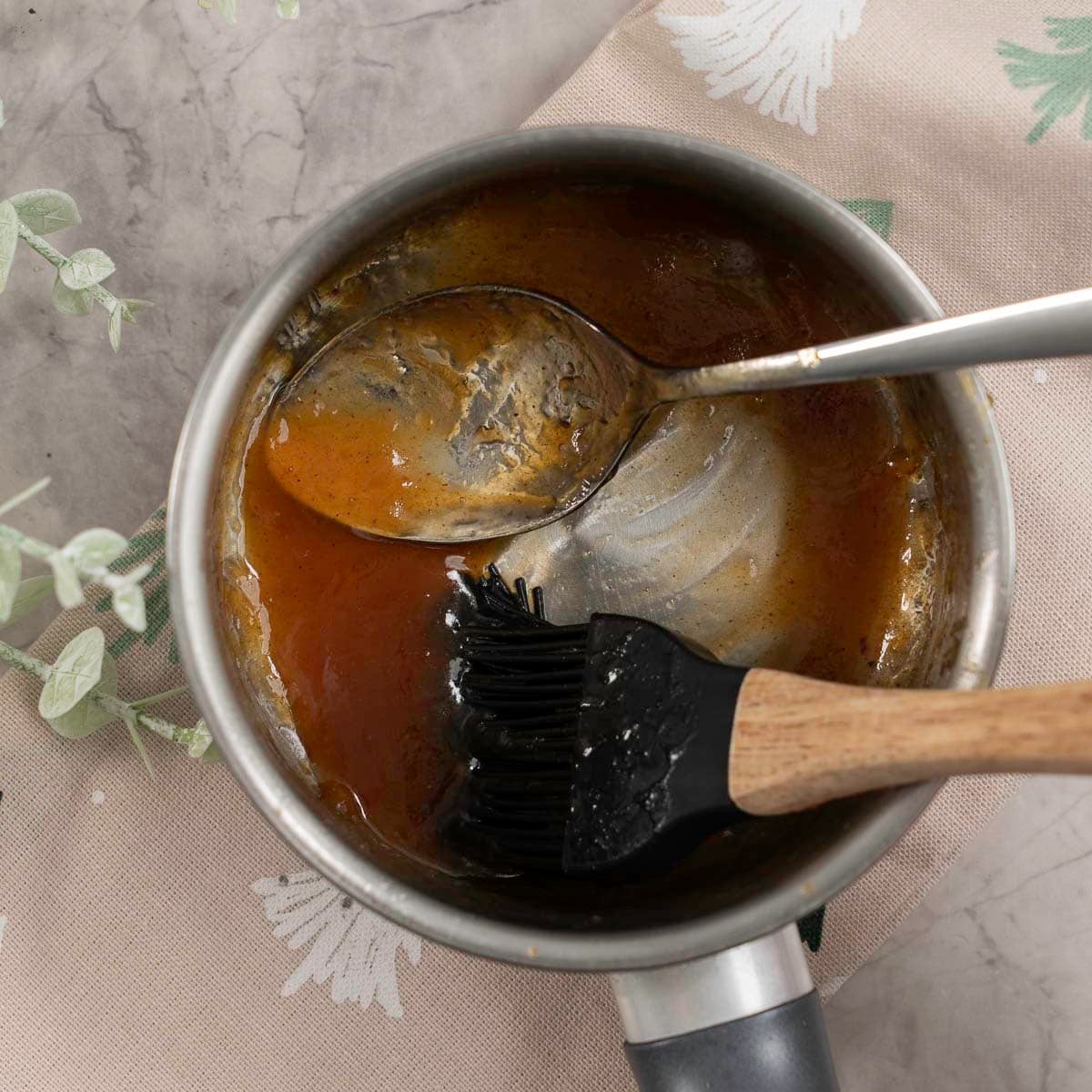 Dessertspoon and basting brush inside a small pot with brown sugar mixture inside.