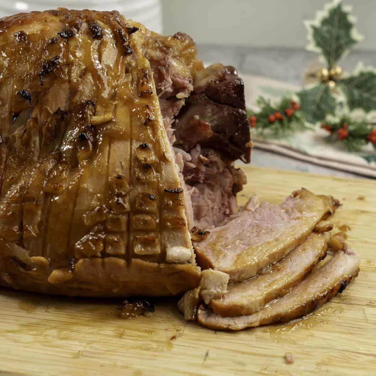Golden glossy ham, three pieces of ham slice onto wooden chopping board.