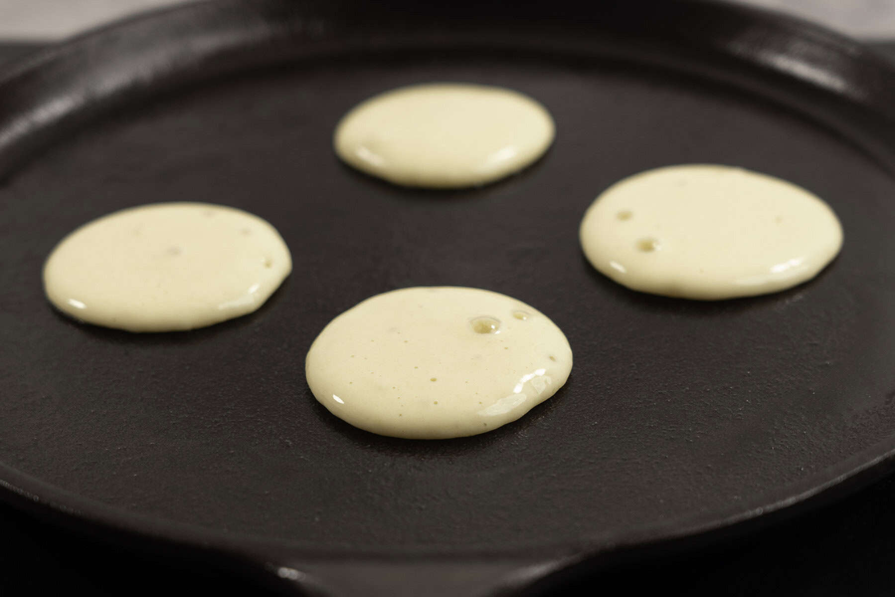Small portions of pancake mixture in a fry pan with bubbles on the top.