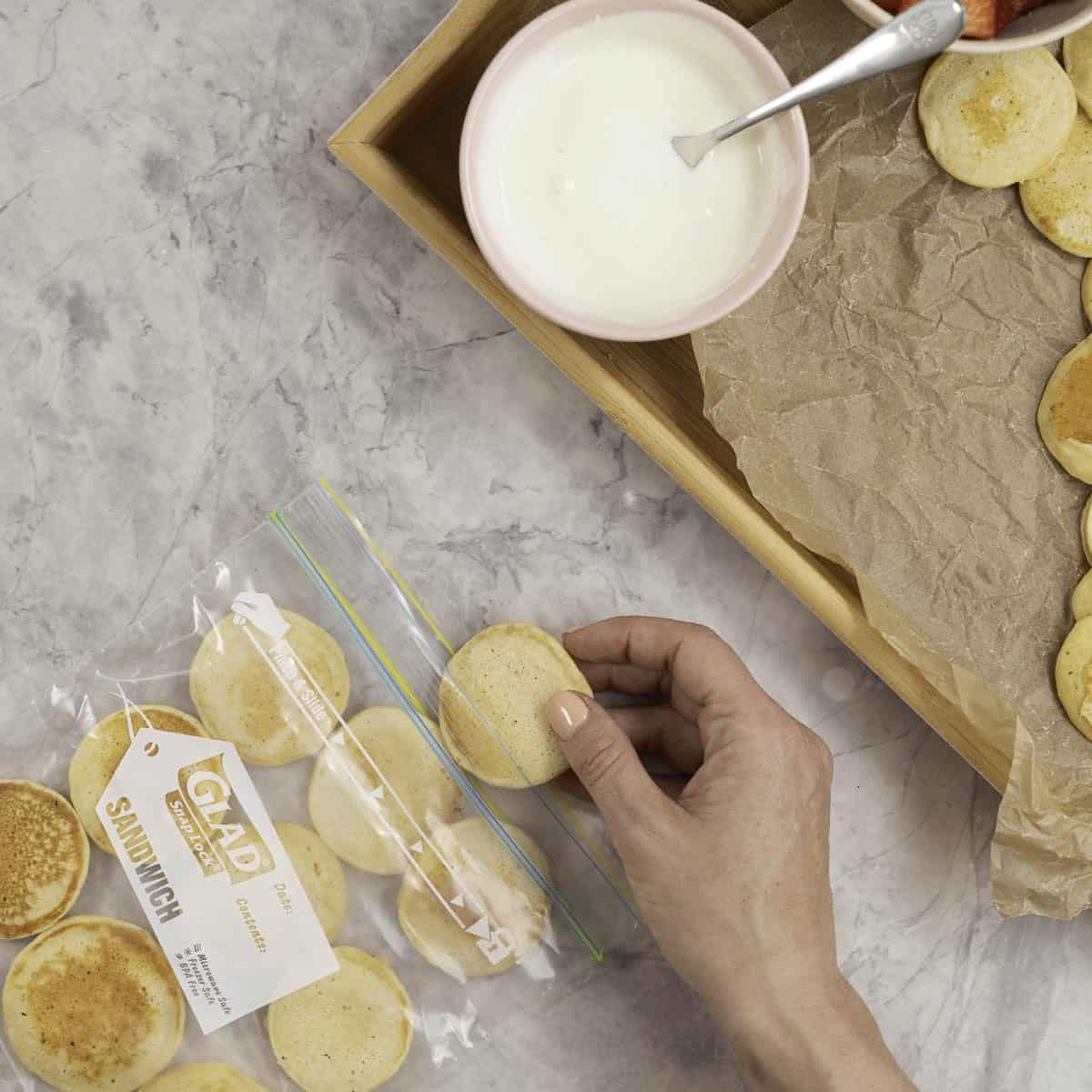 Womans hand placing mini pancake inside a ziplock back.