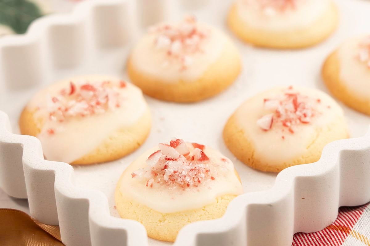 White tray with wavy sides with mint cookies inside decorated with icing and crushed candy cane pieces.