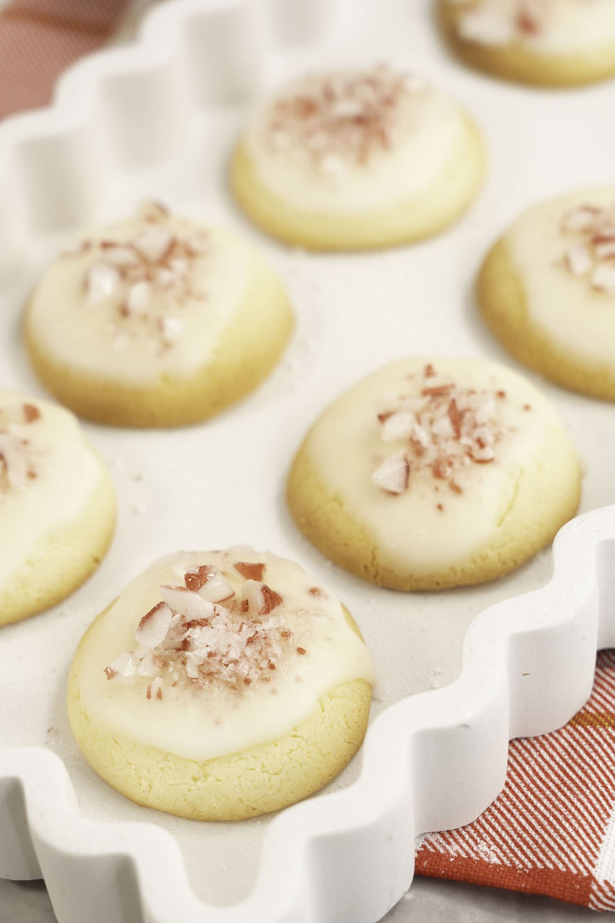 White tray with wavy sides with mint cookies inside decorated with icing and crushed candy cane pieces.