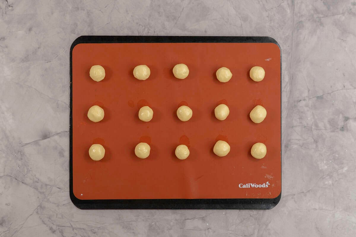 Small dough balls on a silicone cooking sheet on baking tray.