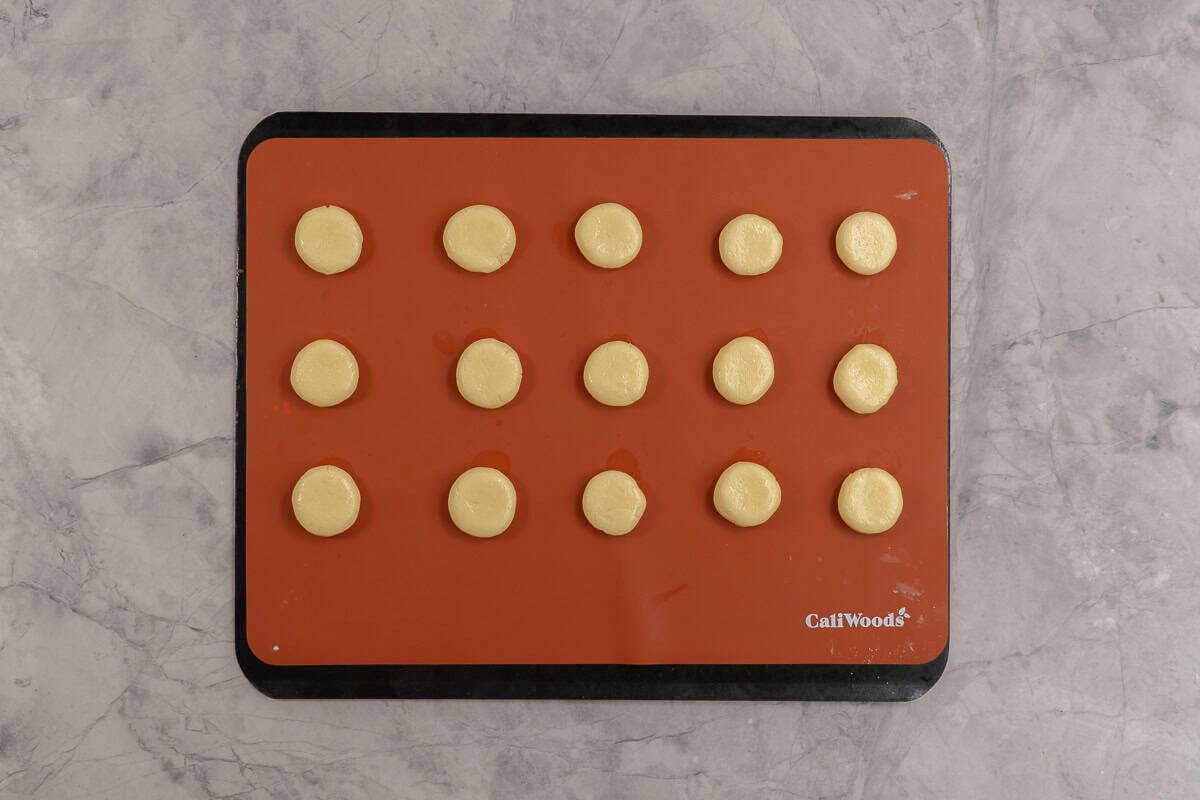 Small dough balls slightly flattened on a silicone cooking sheet on baking tray.