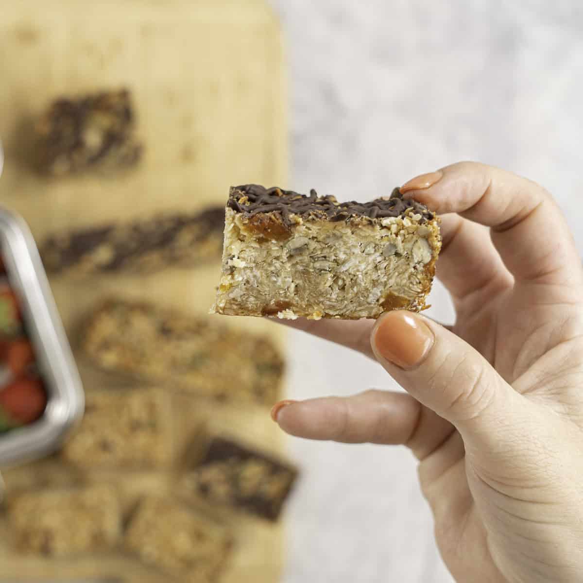 Womans hand holding a small square granola bar showing the inside texture.