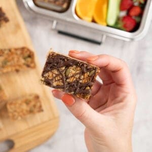 Womans hand holding a small square granola bar with drizzled melted chocolate.