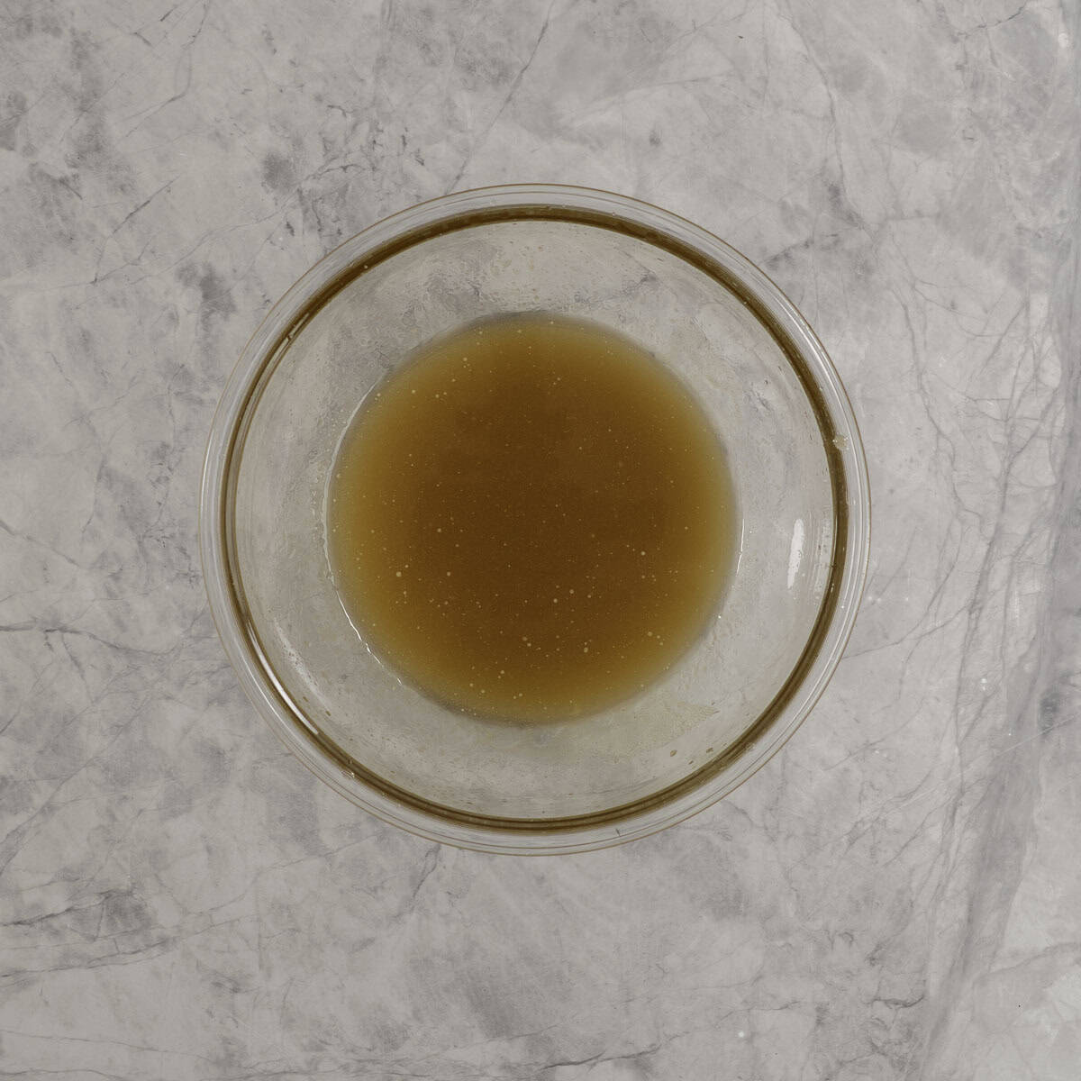 Wet ingredients for granola bars in a large glass bowl on marble bench top.
