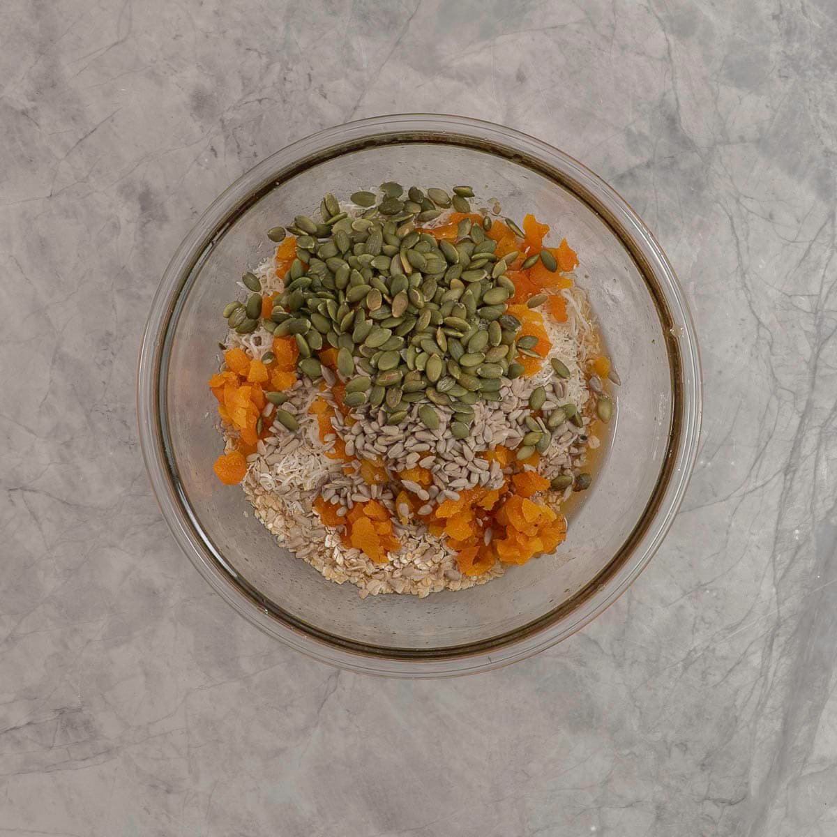 Ingredients for granola bars in a large glass bowl on benchtop.