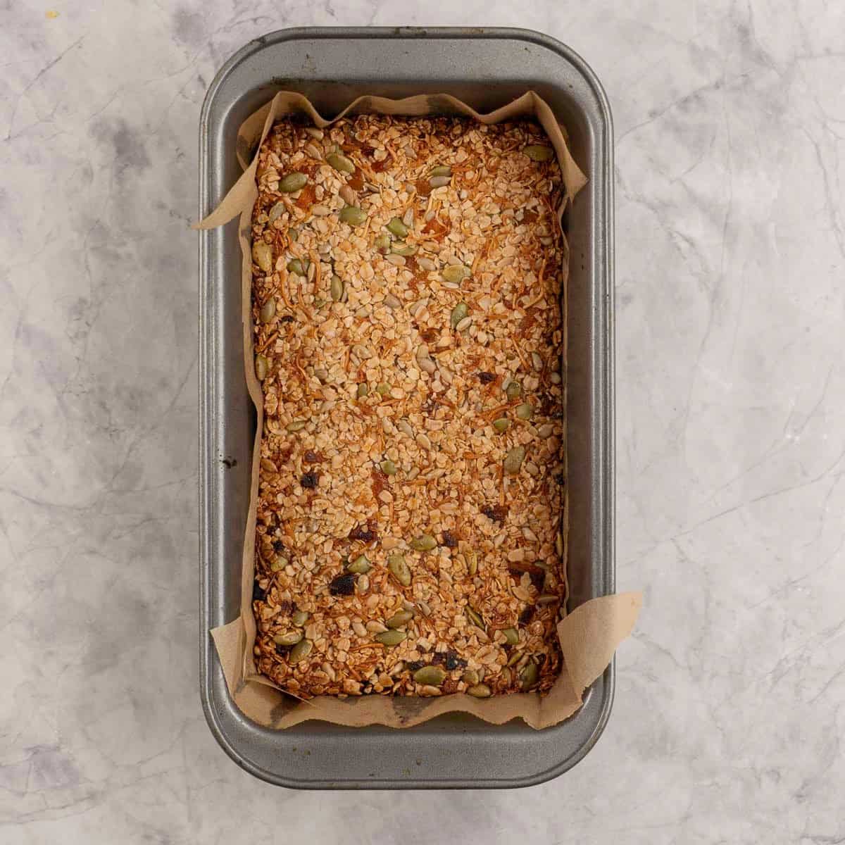 A rectangle lined baking tray with golden granola bars inside