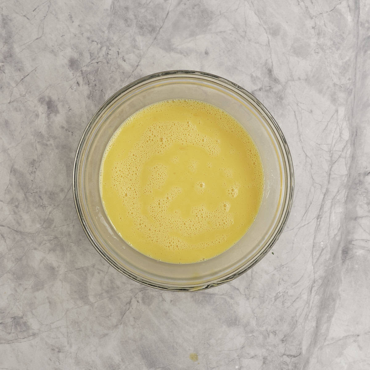 Eggy mixture combined in a large glass bowl on marble bench top.