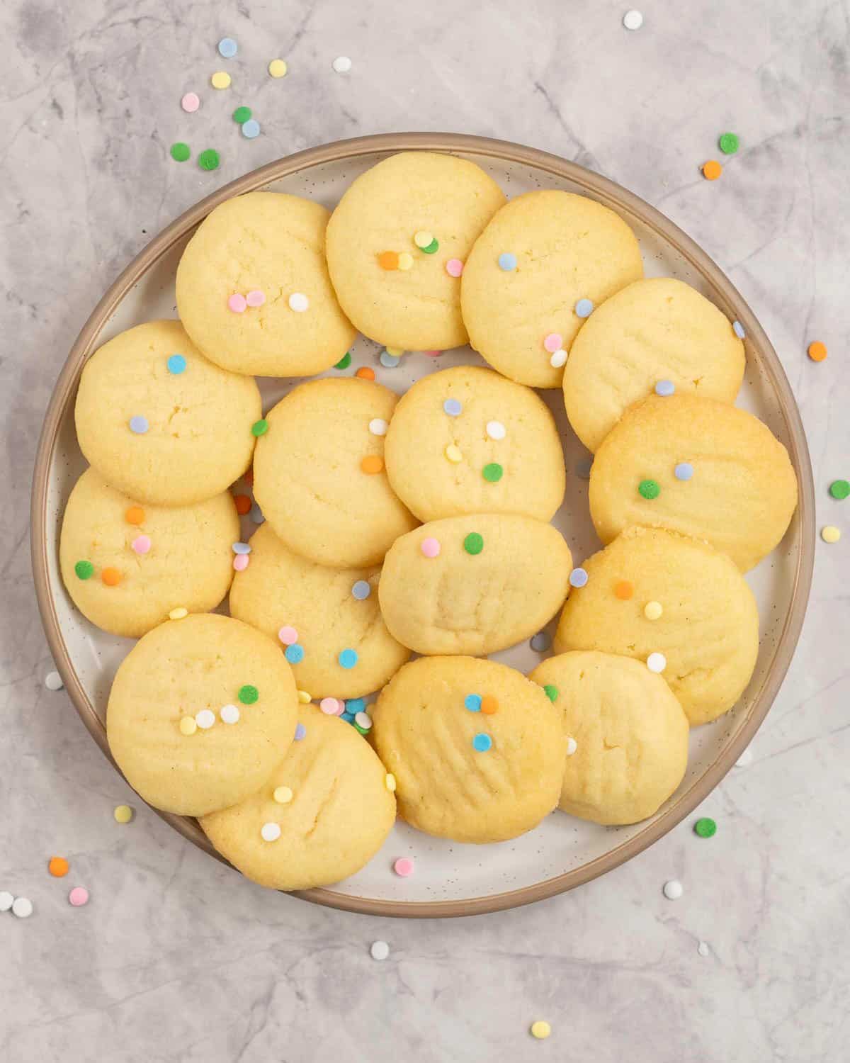 A plate of short bread cookies sprinkled with multi coloured sprinkles.