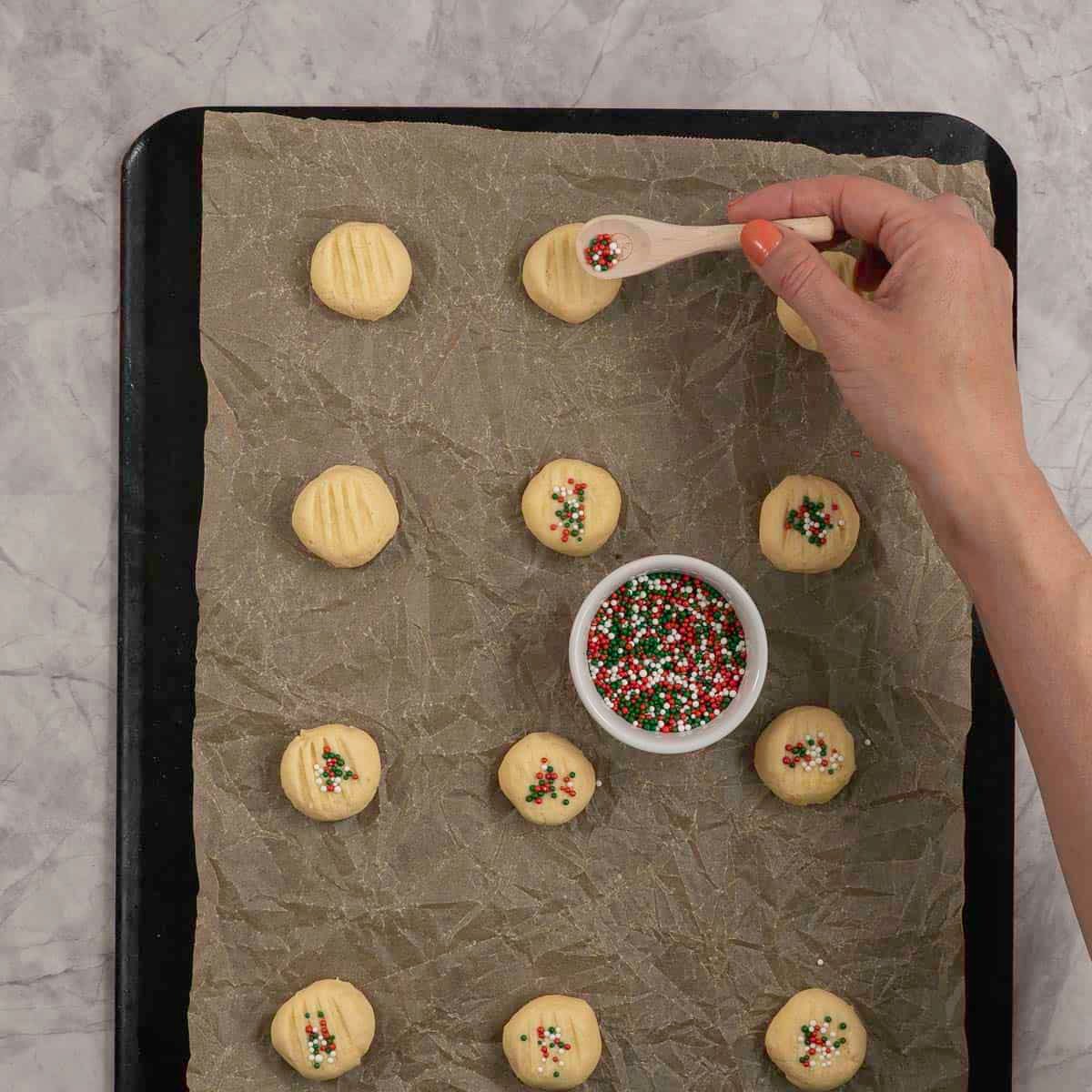 Red green and white sprinkles going on to the top of uncooked shortbread.